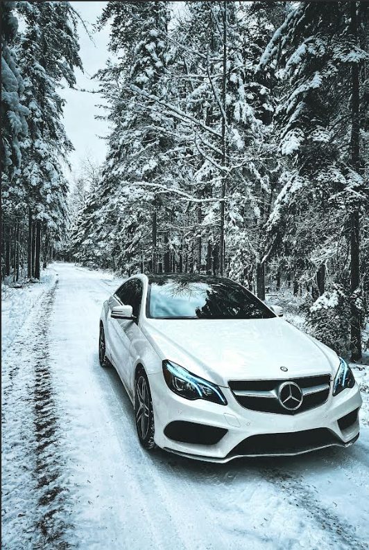 White car parked on a snowy road surrounded by trees